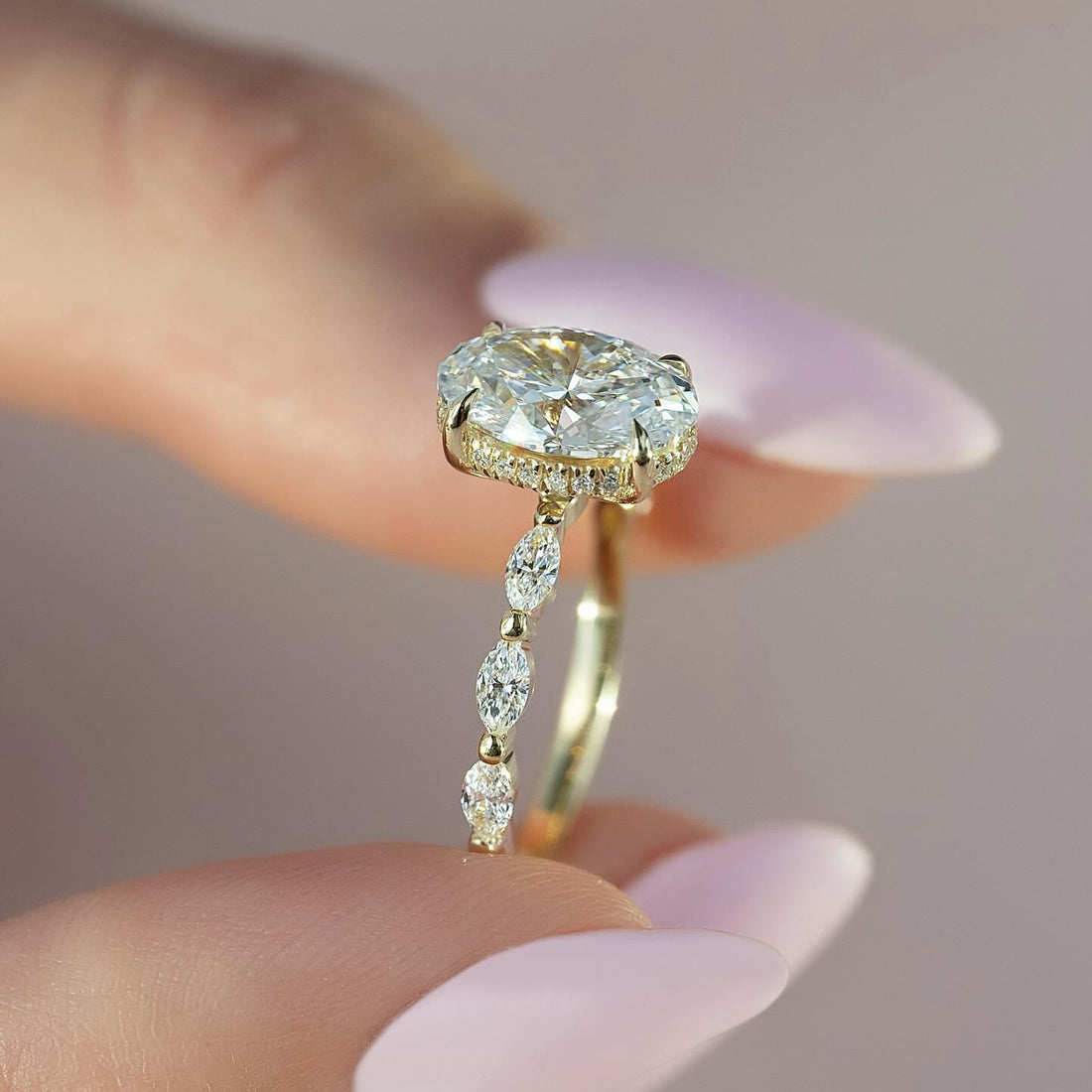 Oval cut lab grown diamond ring in yellow gold with concealed halo and beaded marquise and round accent shank