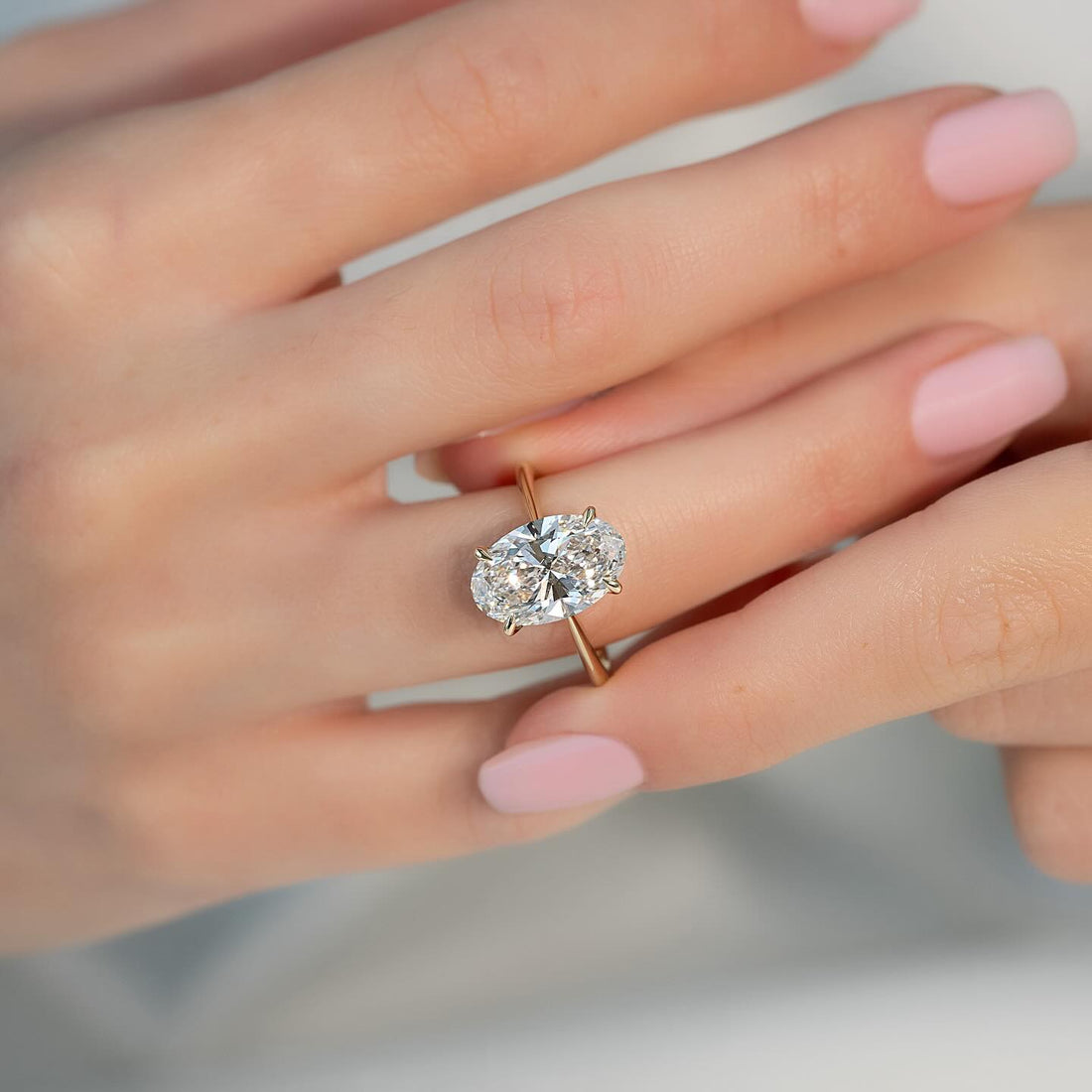 East west oval cut lab grown diamond solitaire ring on a fine rose gold band worn on the hand