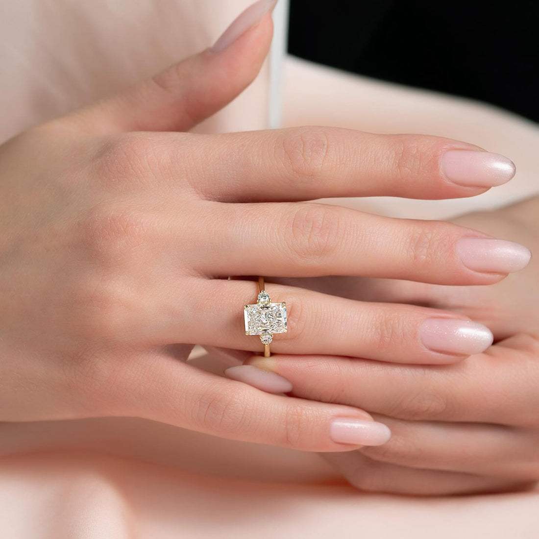East west radiant lab grown diamond ring with round accent shoulders in yellow gold worn on the hand