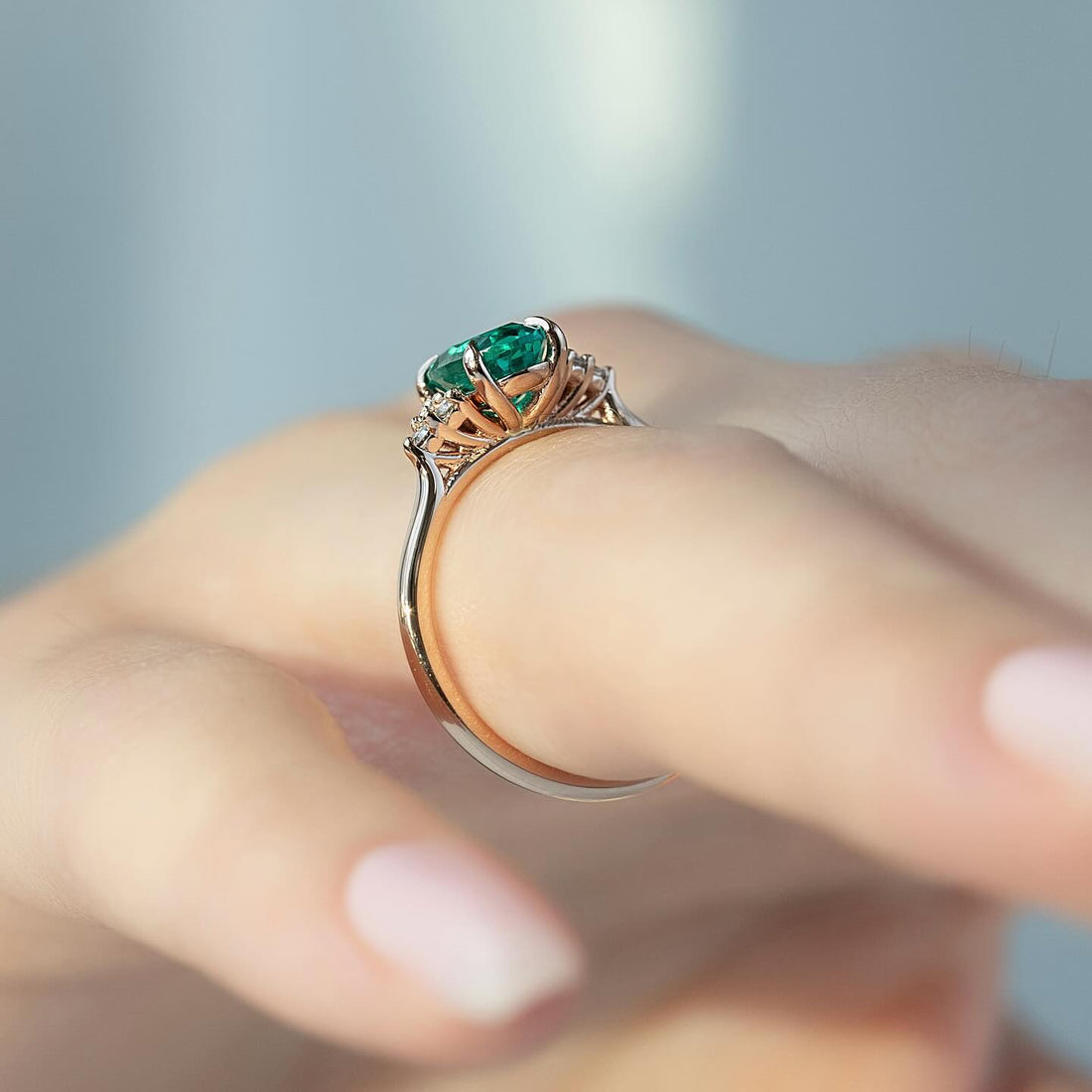 Oval emerald ring with diamond cluster shoulders on a fine two tone band