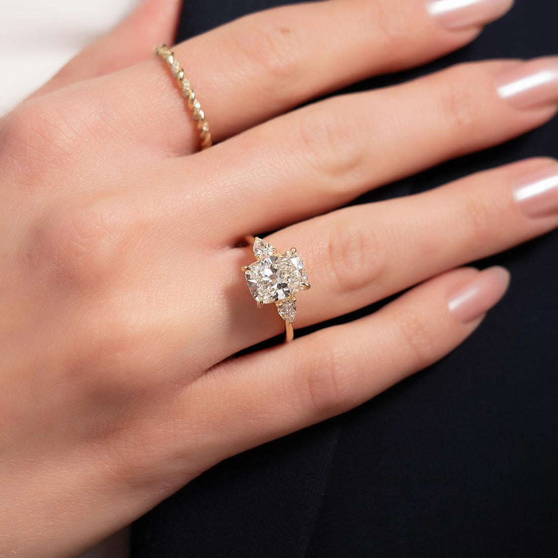 Cushion cut lab grown diamond ring with offset pear side stones in yellow gold worn on the hand