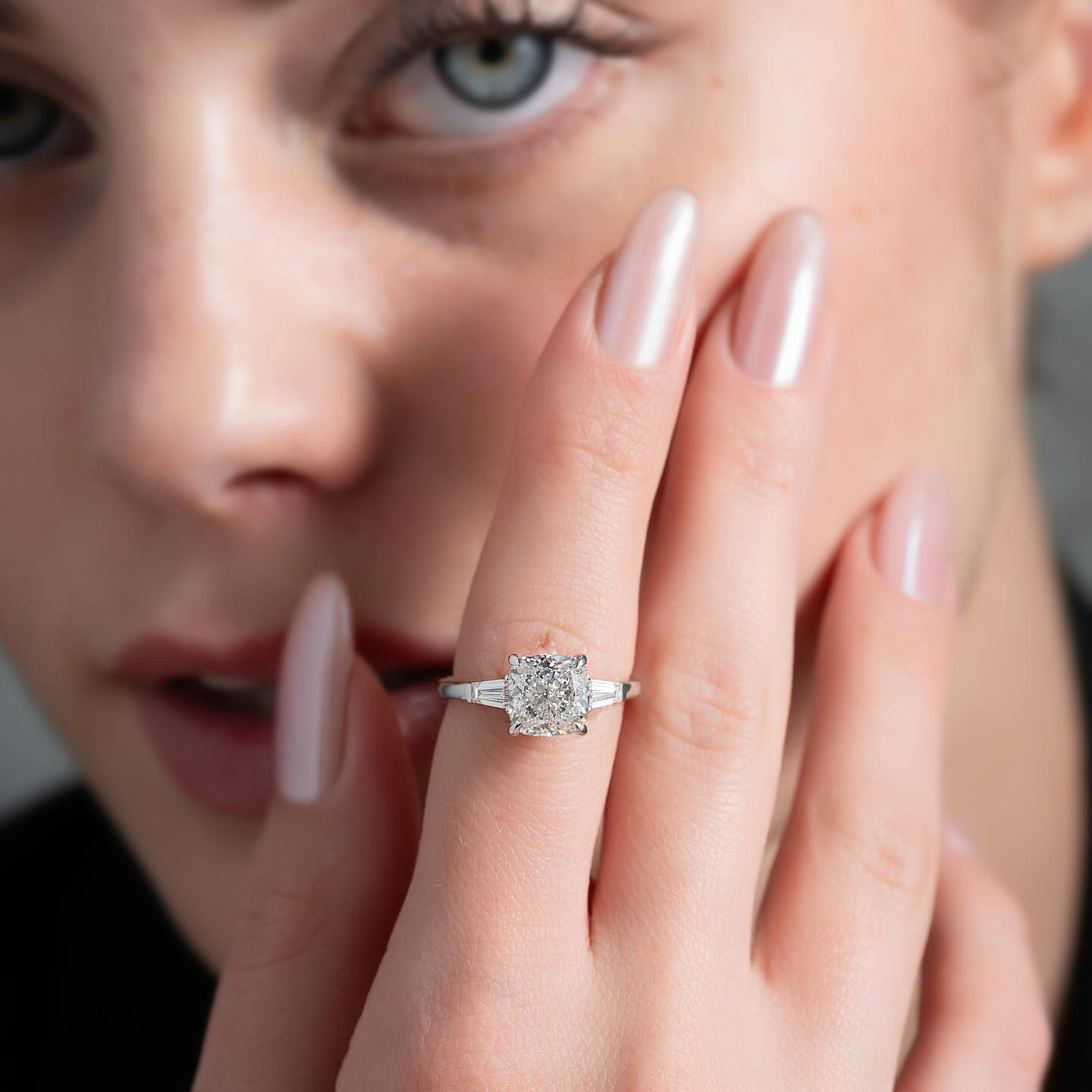 Cushion cut lab grown diamond three stone ring with tapered baguettes in white gold worn on the hand