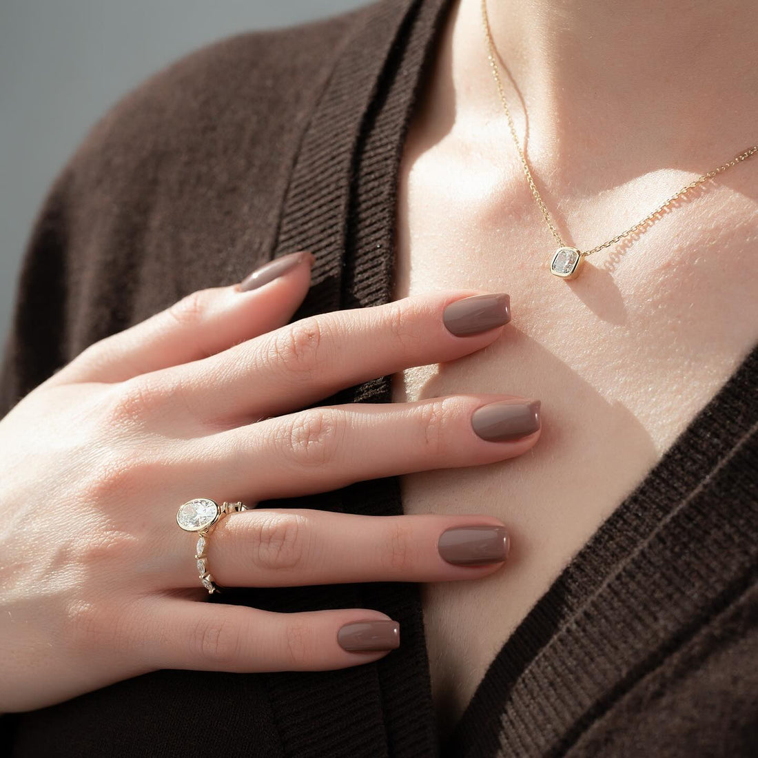 East west bezel set oval lab grown diamond ring with marquise accent band in yellow gold worn on the hand