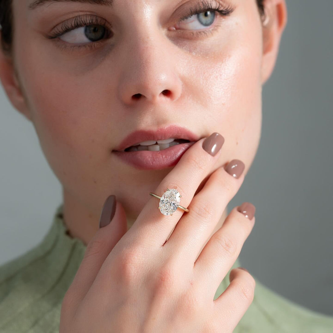 Oval cut lab grown diamond solitaire ring on a slim plain yellow gold band worn on the hand