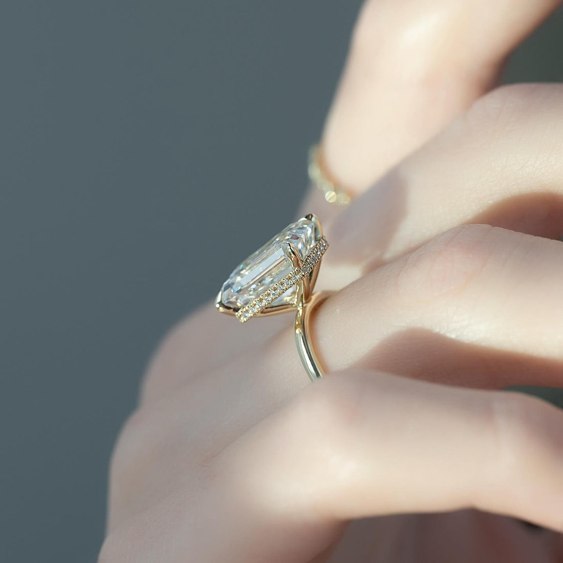 East west emerald cut lab grown diamond ring with concealed halo on a smooth yellow gold shank