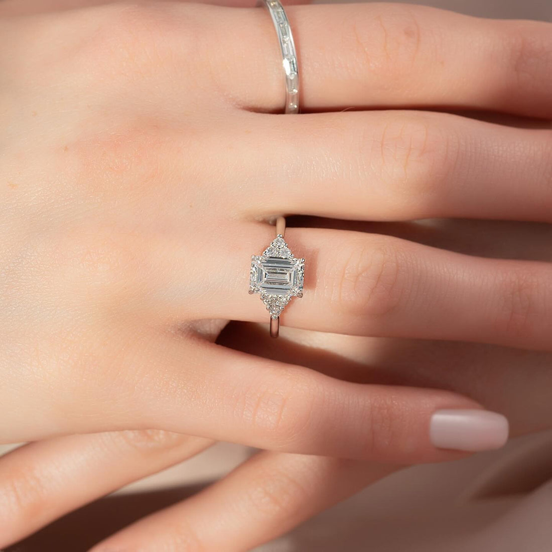 East west emerald cut lab grown diamond ring with accent clusters in white gold worn on the hand