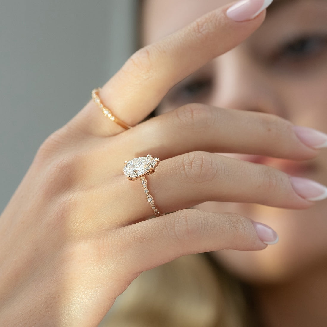 East west oval cut lab grown diamond ring in rose gold on a milgrain station band worn on the hand