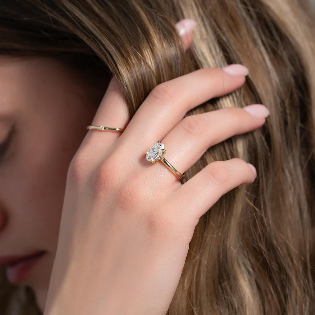 Oval cut lab grown diamond ring with pave hidden halo in yellow gold worn on the hand