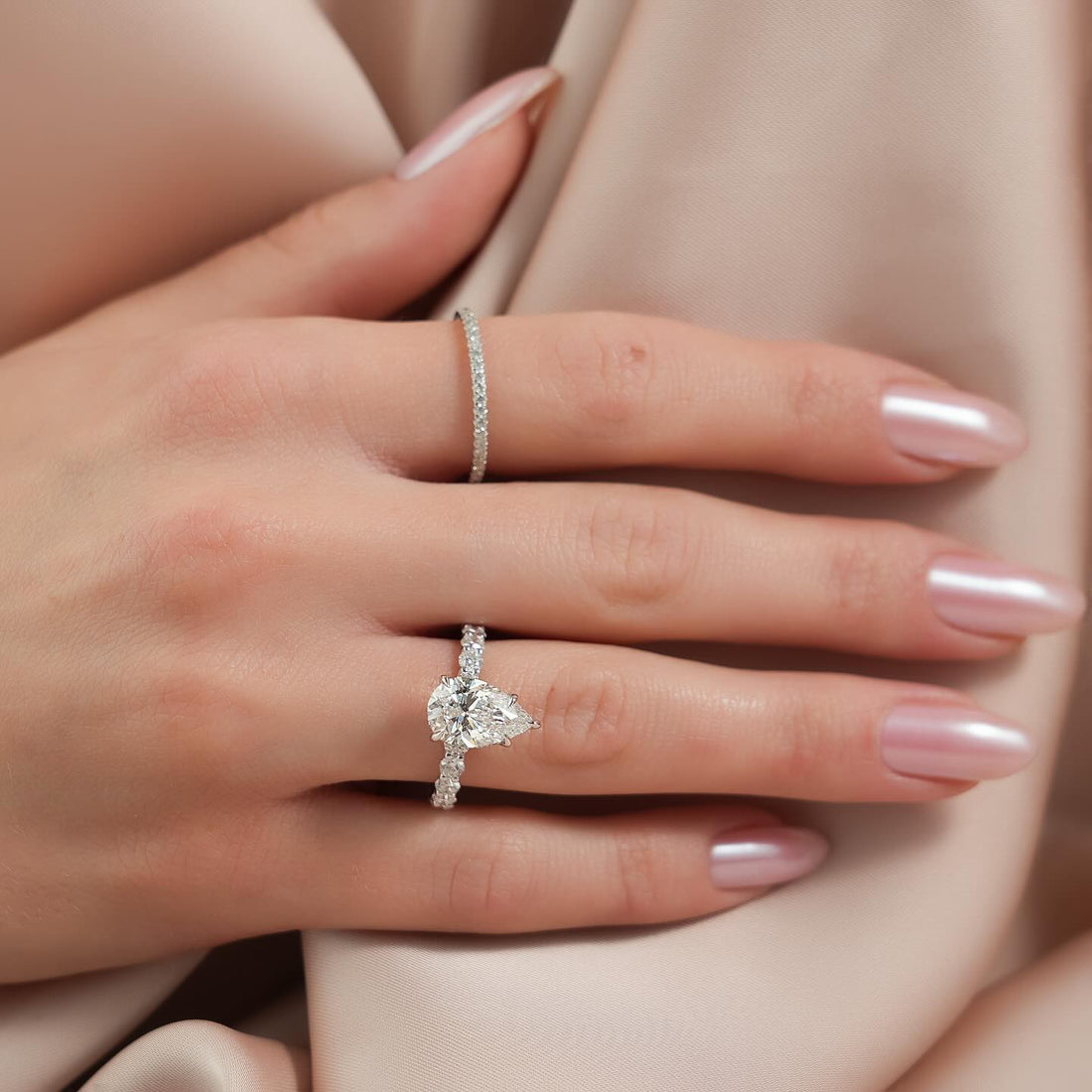 East west pear cut lab grown diamond ring with shared claw diamond band in white gold worn on the hand