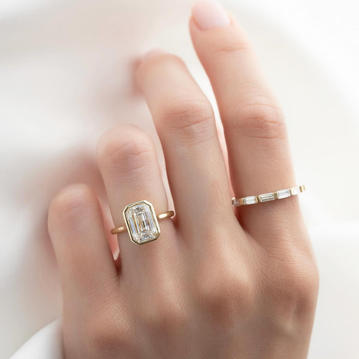 Emerald cut lab grown diamond bezel ring on a fine yellow gold band worn on the hand