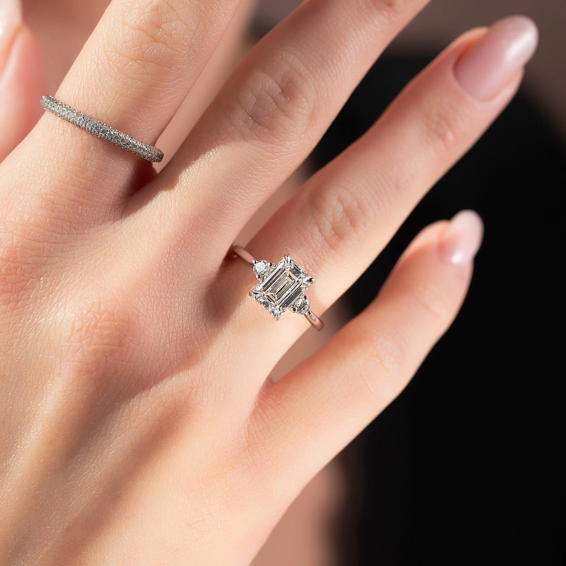 Emerald cut lab grown diamond ring with round corner accents in white gold worn on the hand