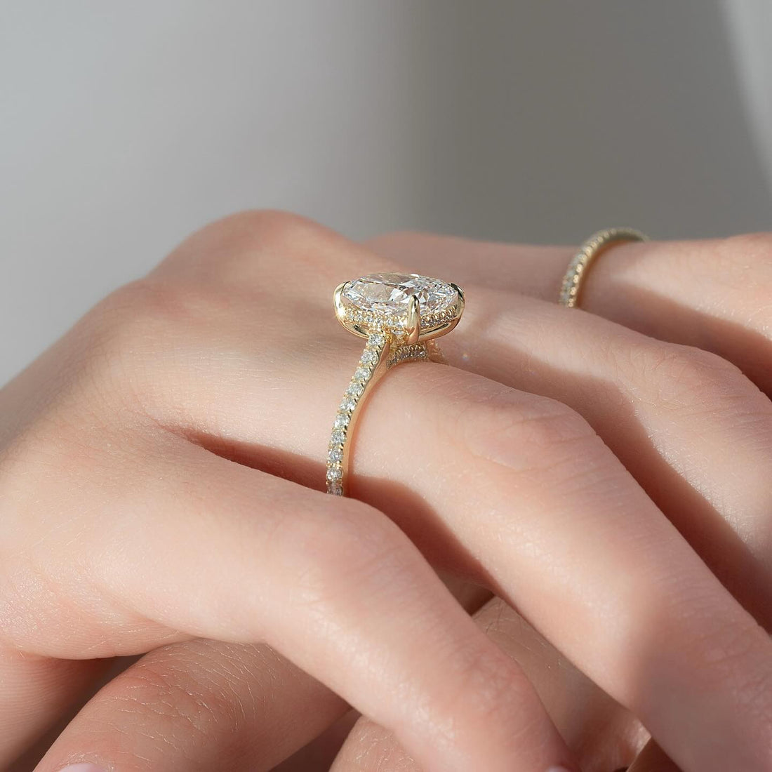 Elongated cushion moissanite hidden halo thin pave ring on hand in yellow gold