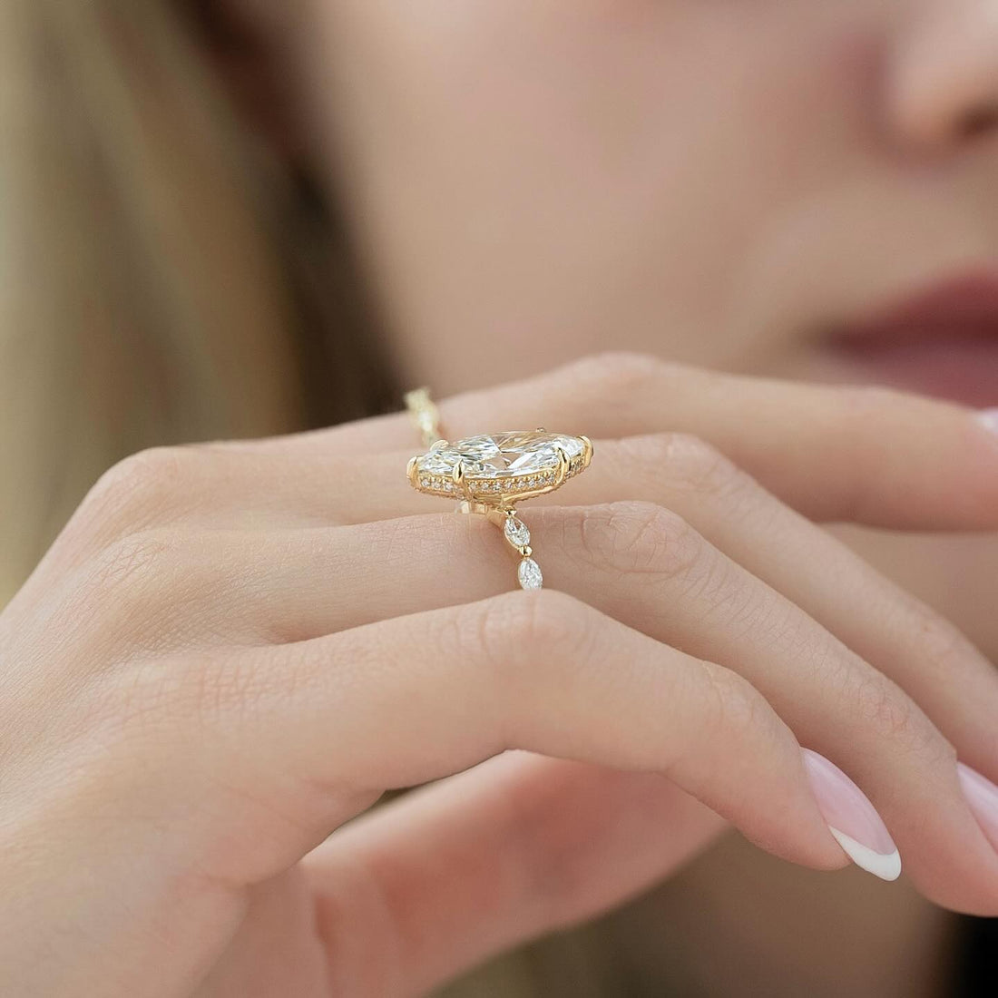 Marquise moissanite ring with spaced marquise accent band held in fingers in yellow gold