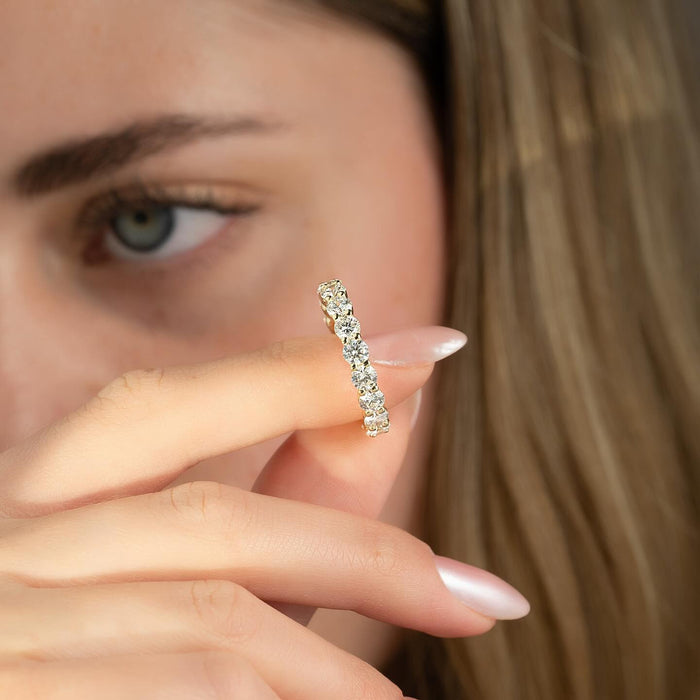 Round moissanite shared prong full eternity band held in fingers in yellow gold