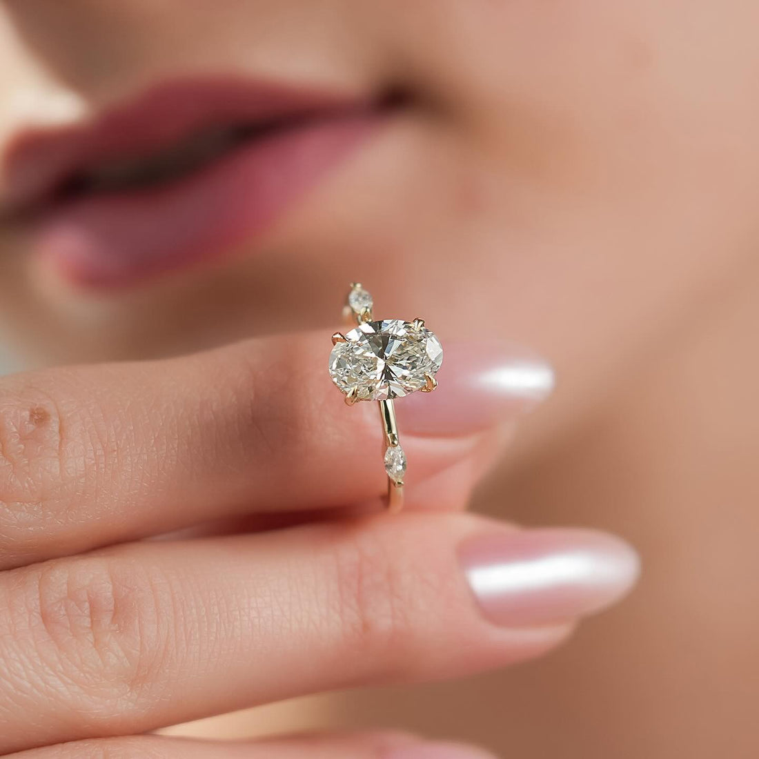 Oval moissanite hidden halo marquise side accent ring held in fingers in yellow gold