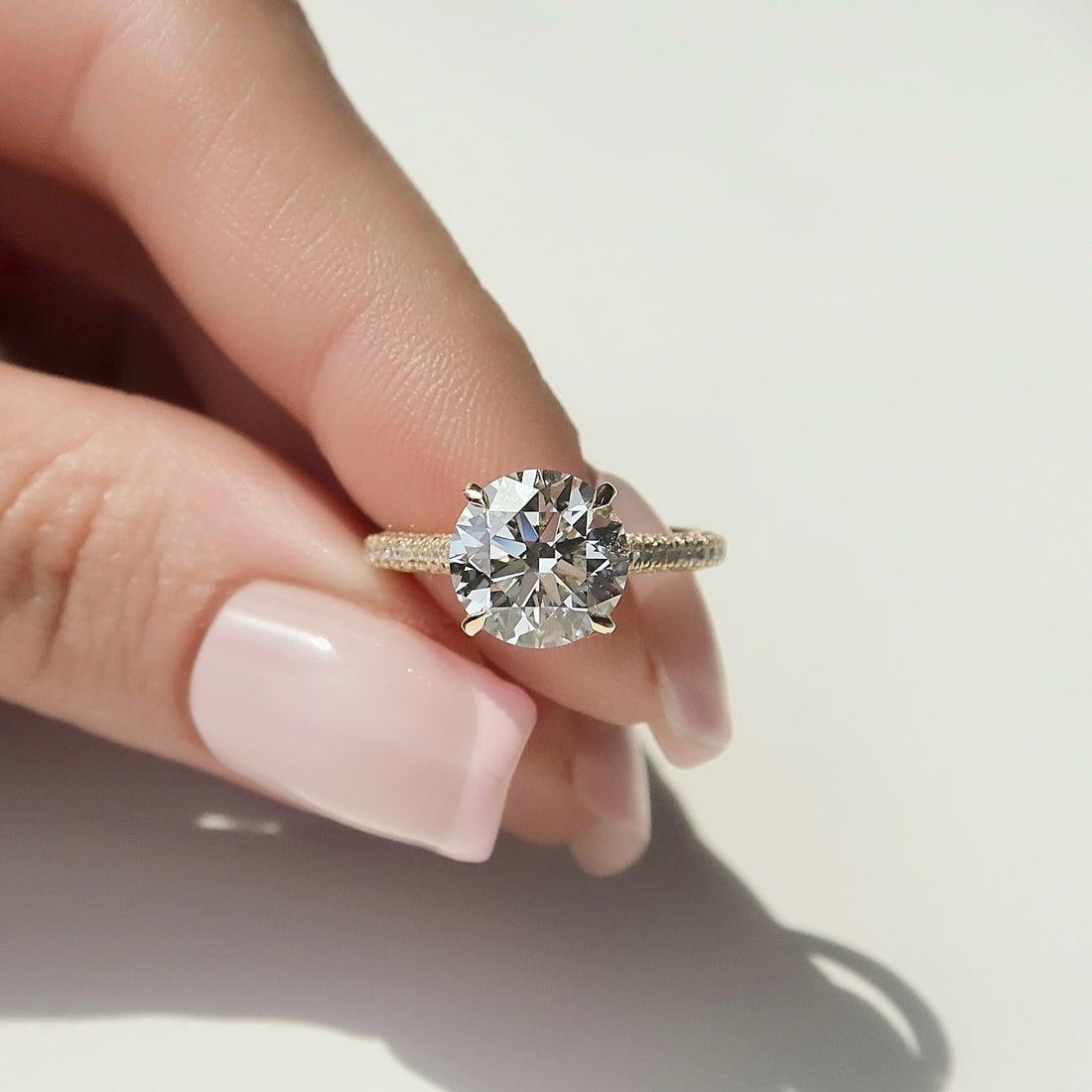 Round moissanite hidden halo three sided pave ring worn on hand in yellow gold