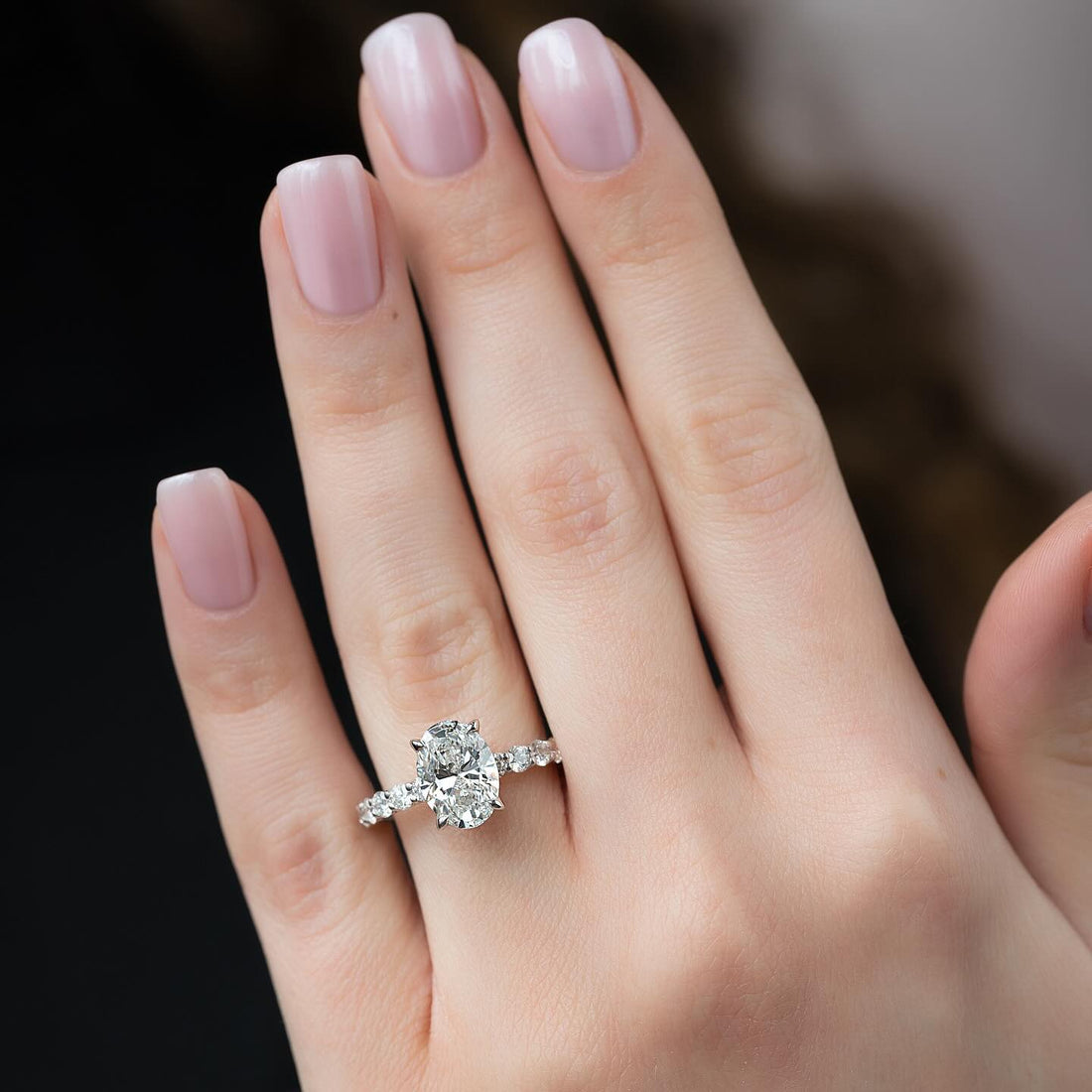 Oval moissanite shared prong accent band ring worn on hand in white gold