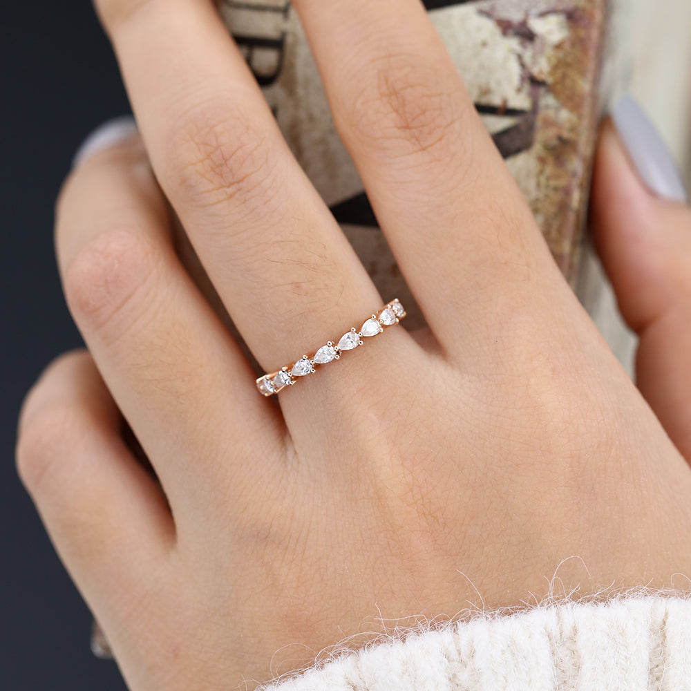 Rose gold pear moissanite half eternity band worn on a finger holding a book
