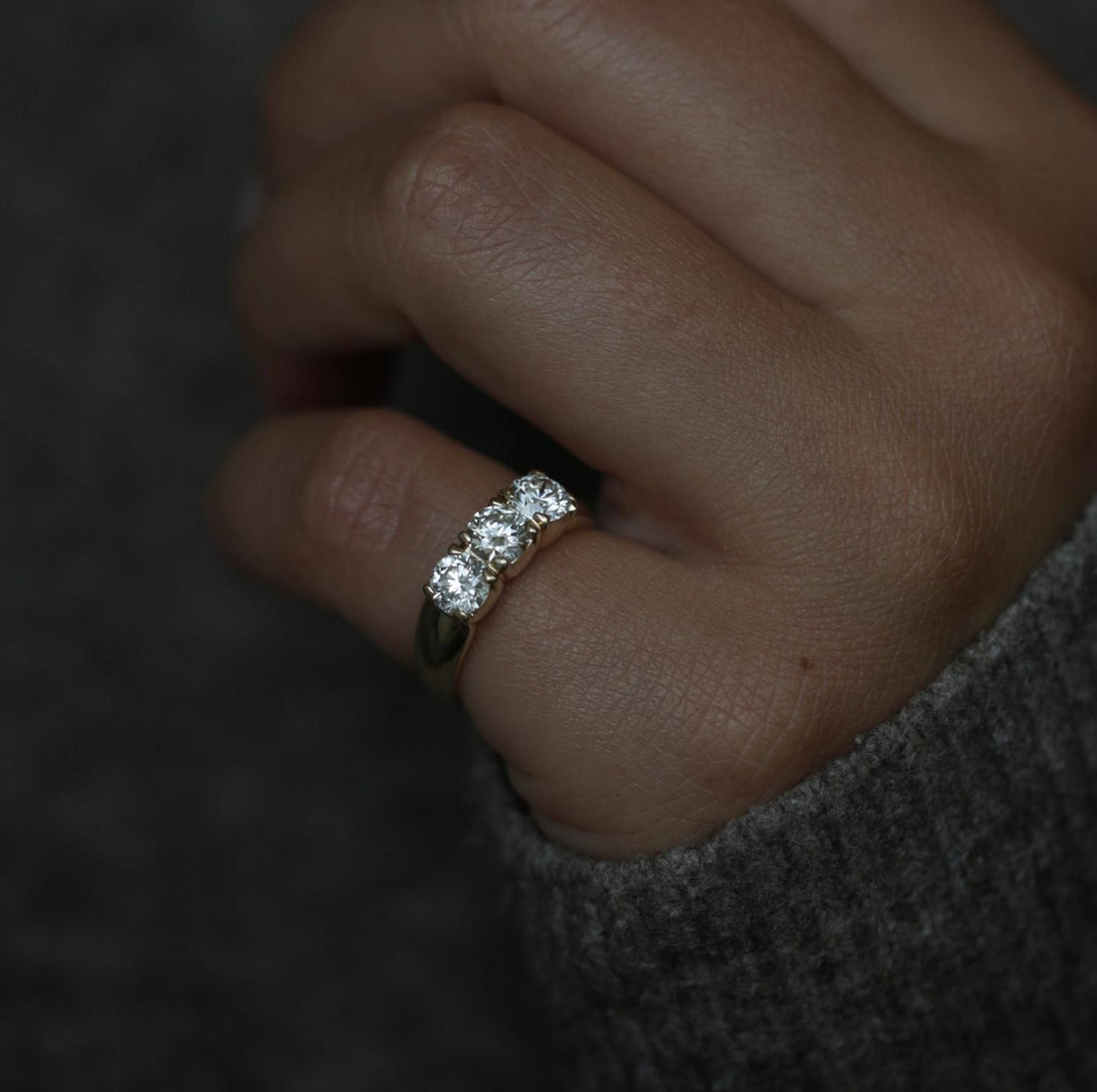 Round three stone lab grown diamond wedding band in yellow gold worn on a hand against a grey sleeve