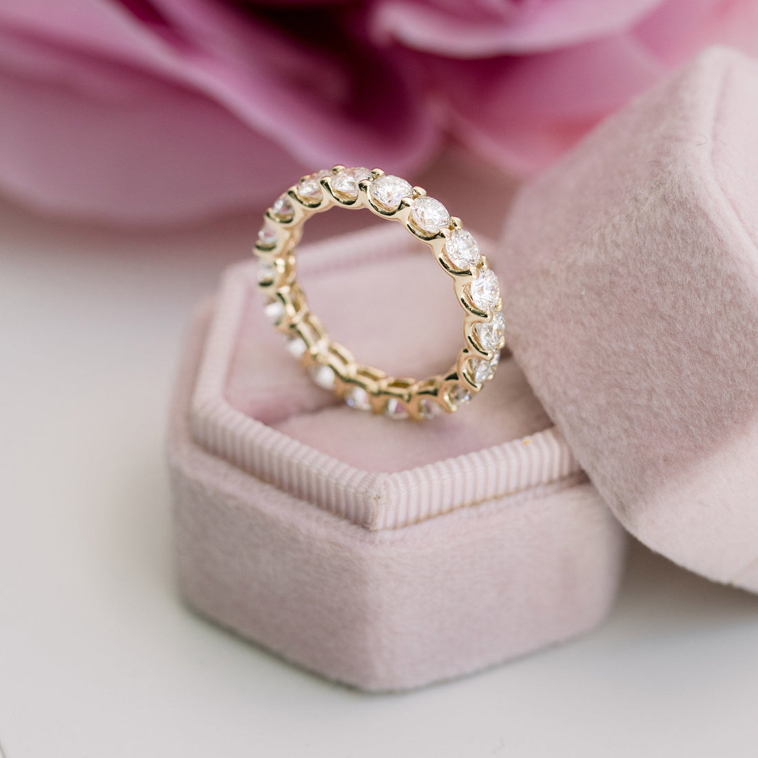 Yellow gold round moissanite full eternity band standing in a pink velvet ring box