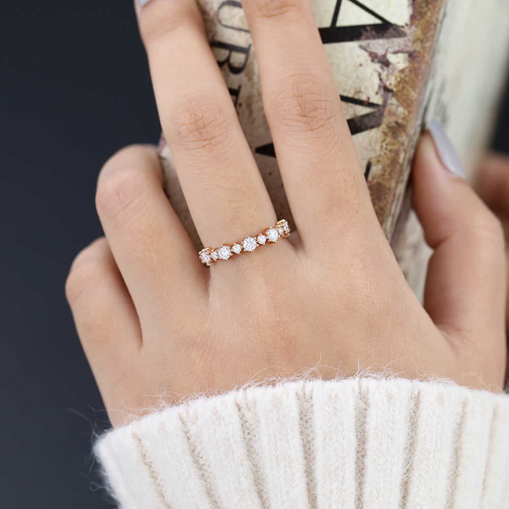 Round moissanite alternating size half eternity wedding band in rose gold worn on the finger