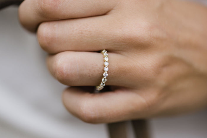 Side view of a bubble prong round moissanite wedding band in yellow gold on a hand