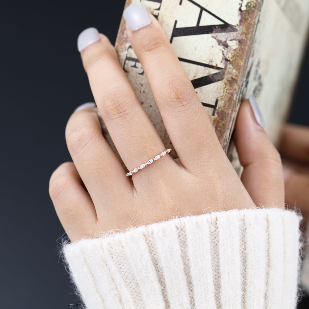 Rose gold marquise moissanite eternity band worn on a finger holding a book