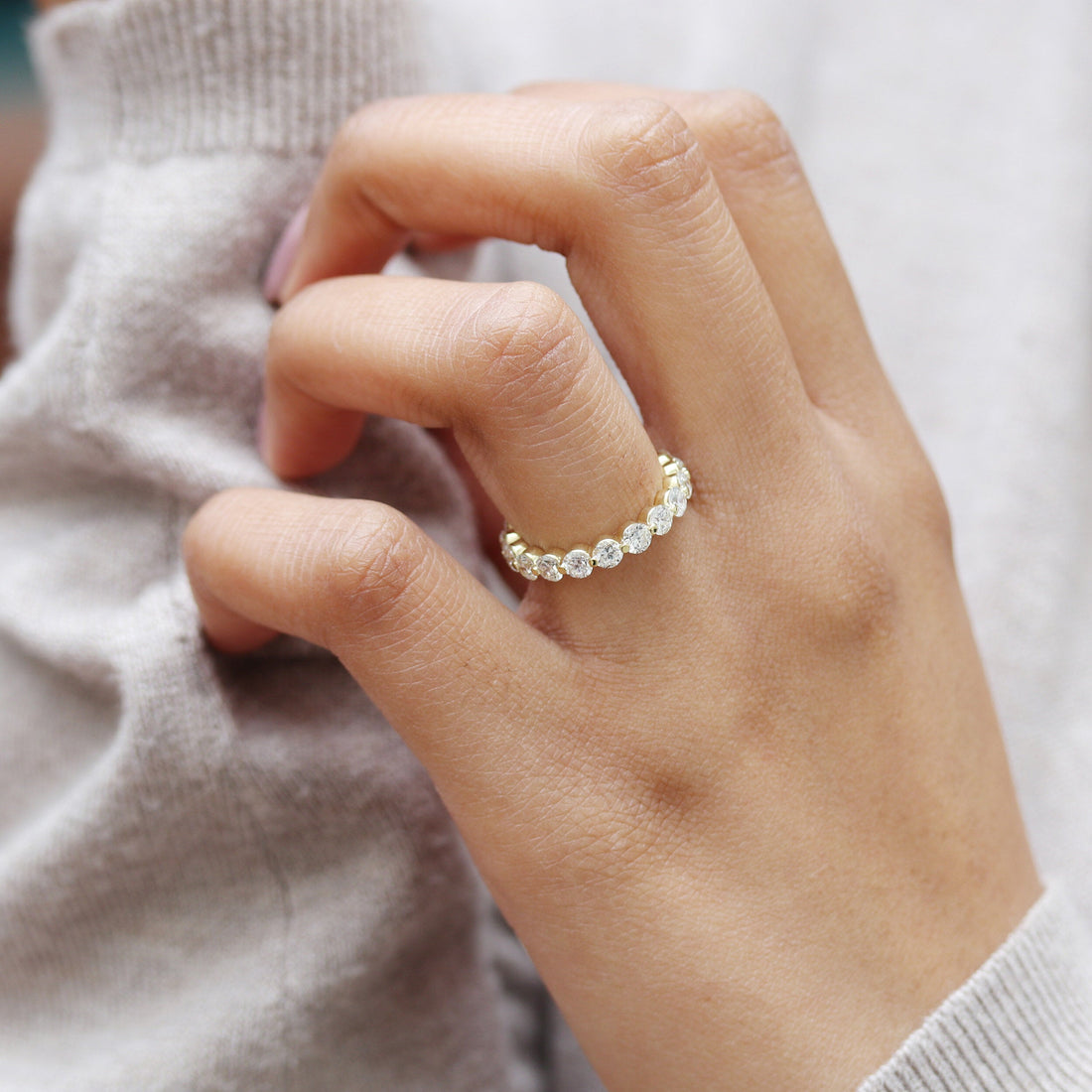 Yellow gold single prong moissanite three quarter eternity band worn on a finger