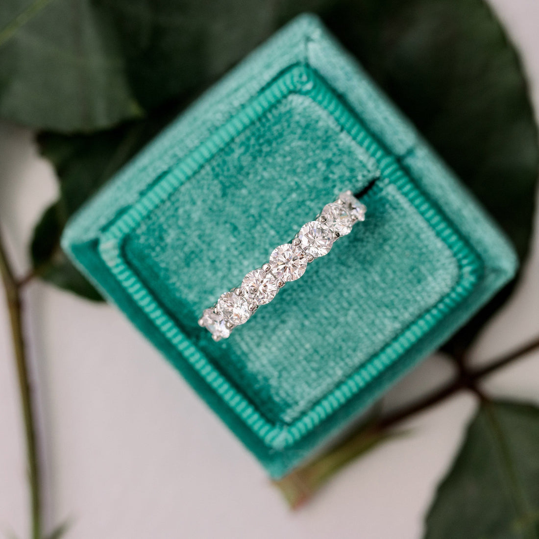 White gold seven stone moissanite band in a green velvet ring box