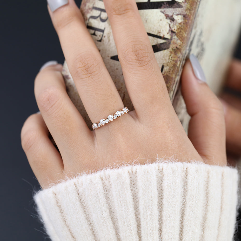 Rose gold round moissanite band with alternating large and small stones worn on a finger holding a book