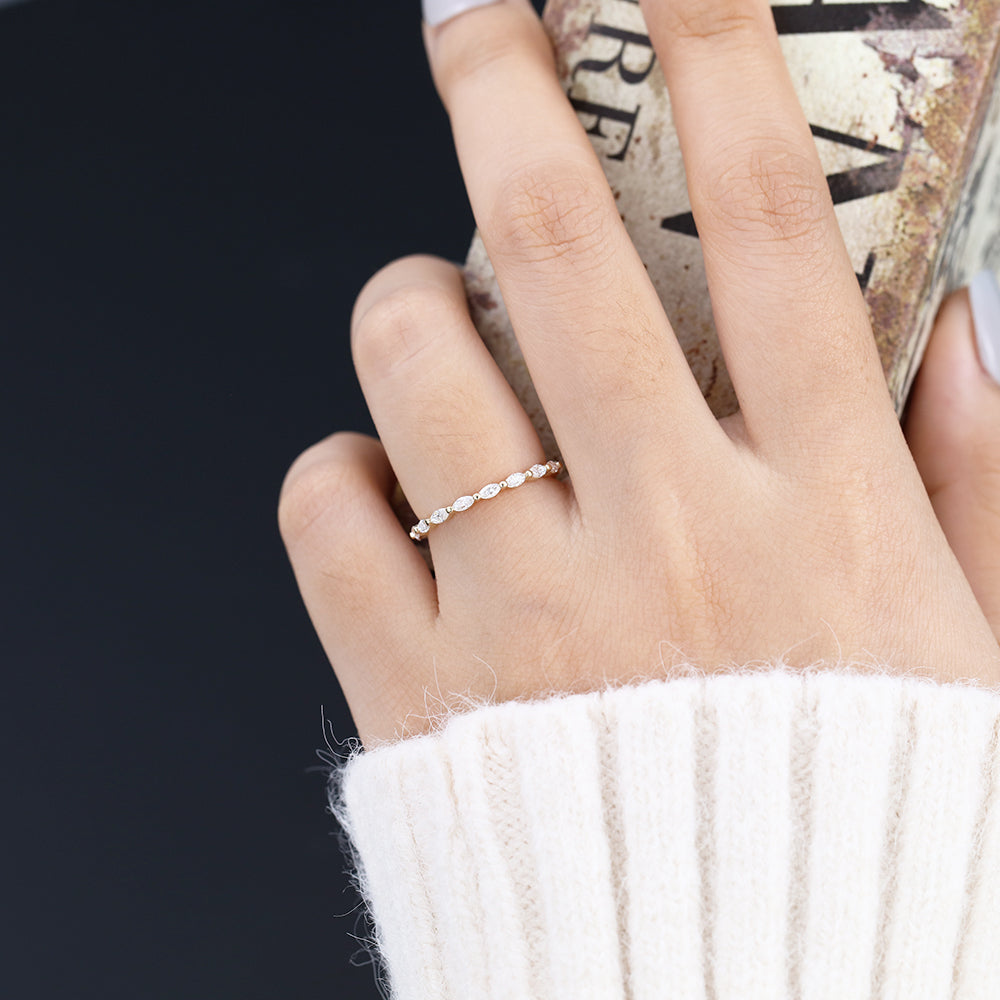 Yellow gold marquise moissanite eternity band worn on a finger holding a book