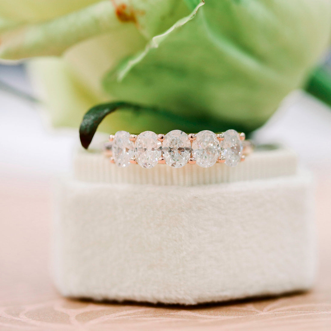Rose gold oval moissanite five stone wedding band standing on a ring box
