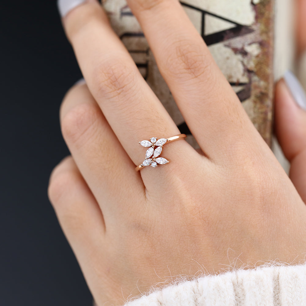 Rose gold leaf cluster moissanite band with marquise stones worn on a finger holding a book