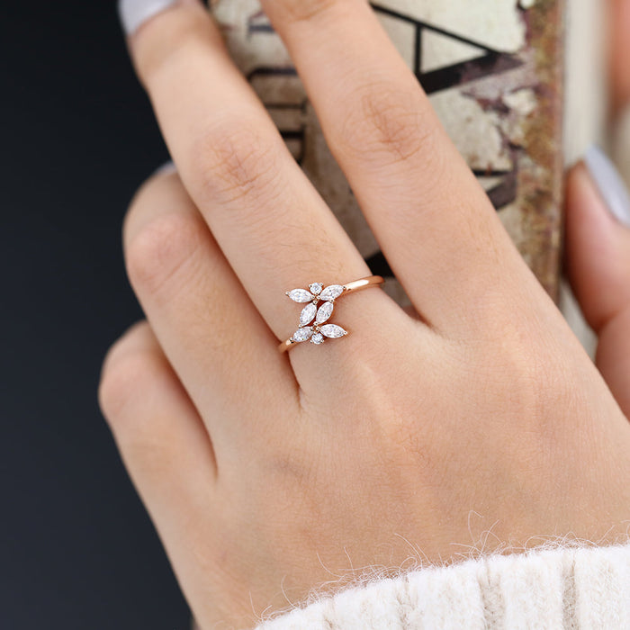 Rose gold leaf cluster moissanite band with marquise stones worn on a finger holding a book