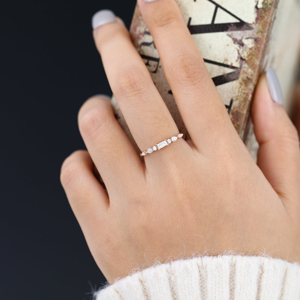 Rose gold multi stone moissanite band with a baguette center worn on a finger holding a book
