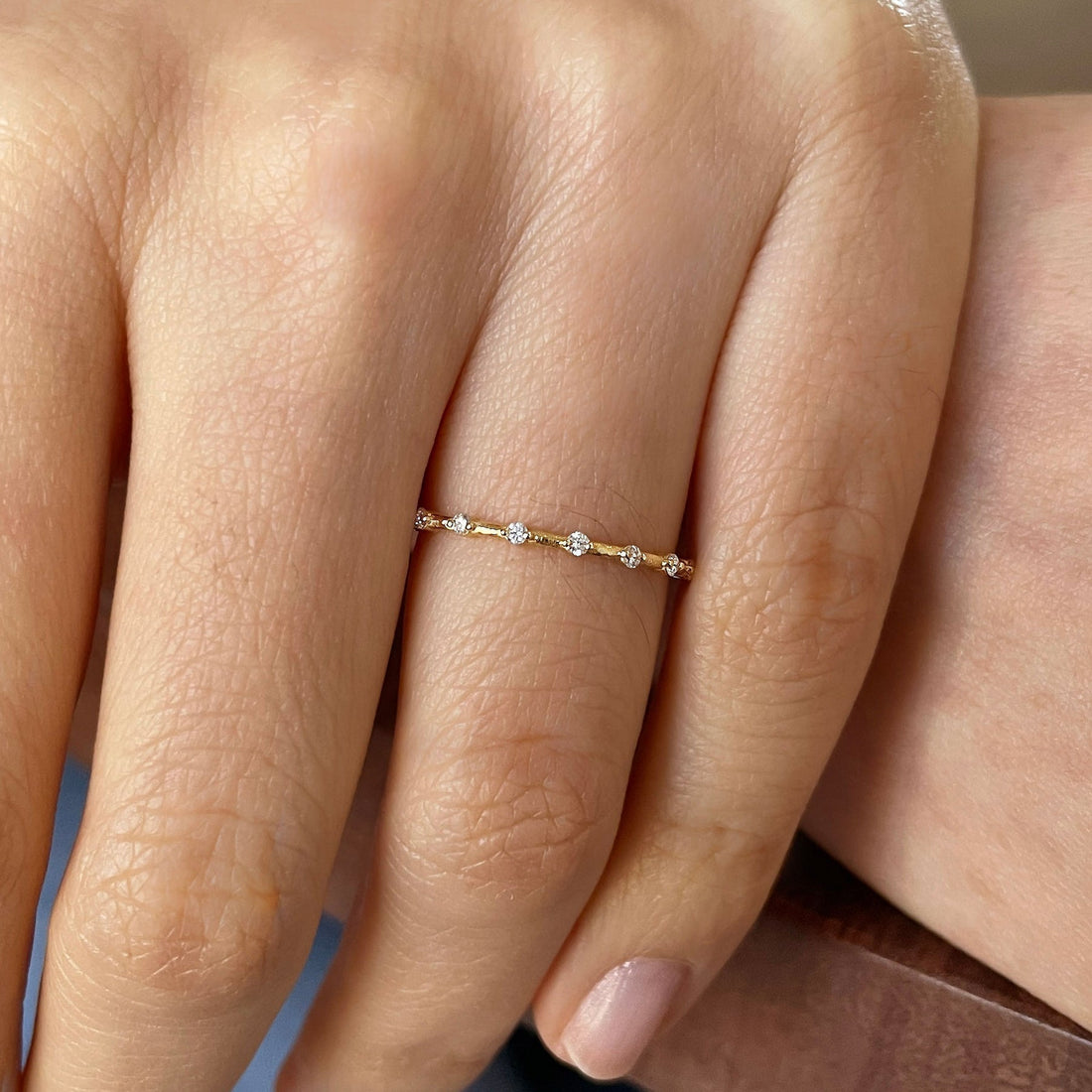 Dainty round lab grown diamond wedding band in yellow gold worn on a finger