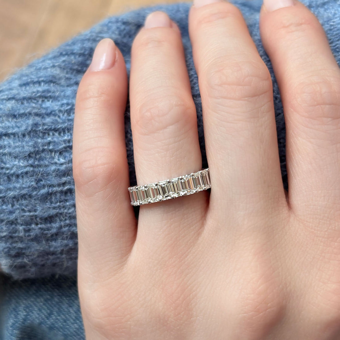 Emerald cut lab grown diamond full eternity wedding band worn on a hand with a blue knit sweater