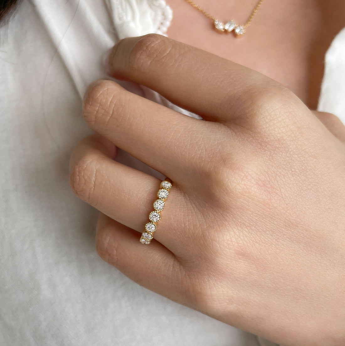 Round lab grown diamond milgrain bezel wedding band in yellow gold worn with a gold necklace