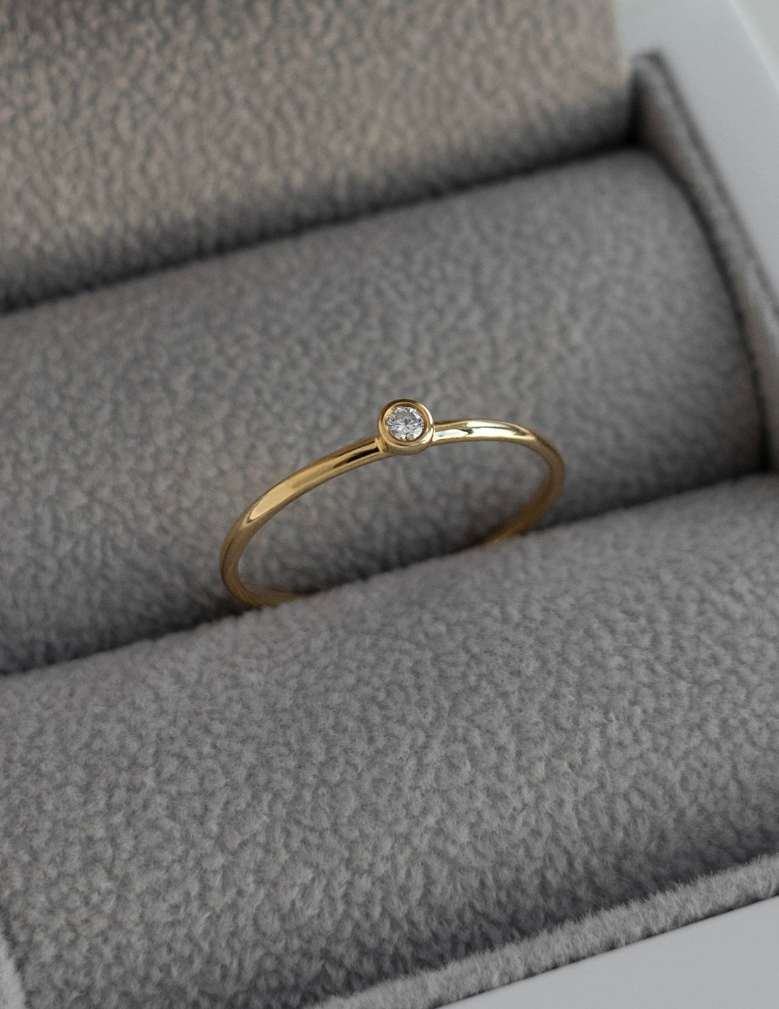 Slim gold stacking ring with one small bezel set round moissanite in a ring box
