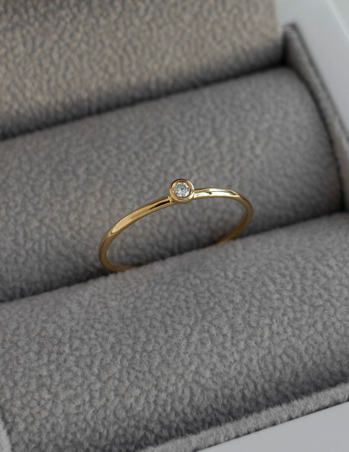 Slim gold stacking ring with one small bezel set round moissanite in a ring box