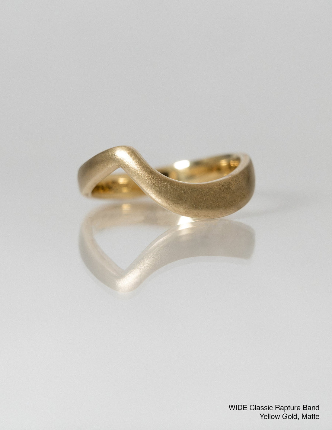 Wide plain gold arc wedding band with a matte finish on a white surface