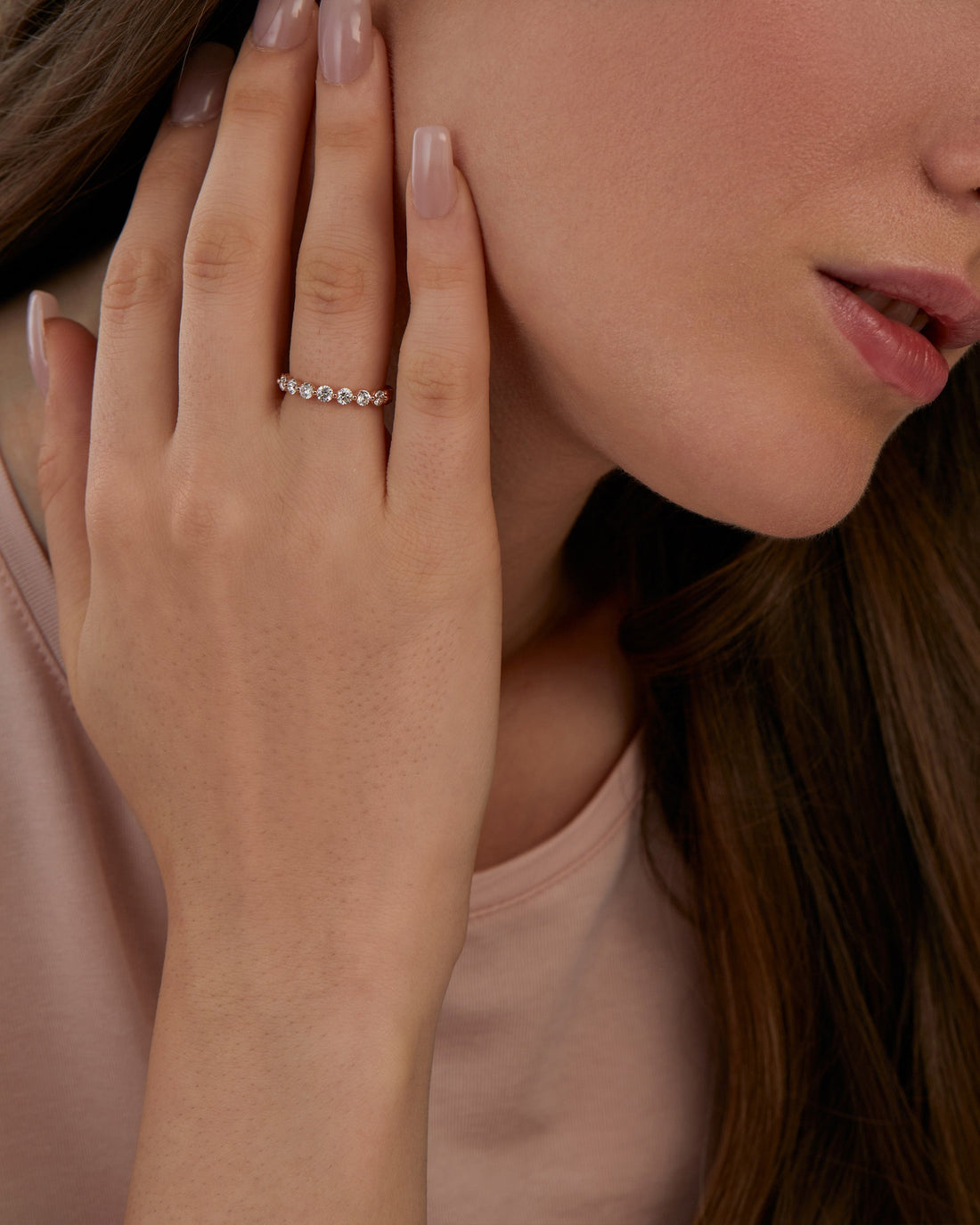 Round full eternity lab grown diamond wedding band in rose gold worn on a hand near the face