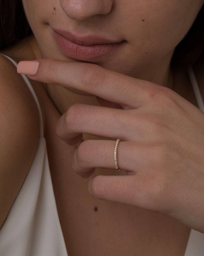 Slim round half eternity pave moissanite wedding band in yellow gold worn on the ring finger
