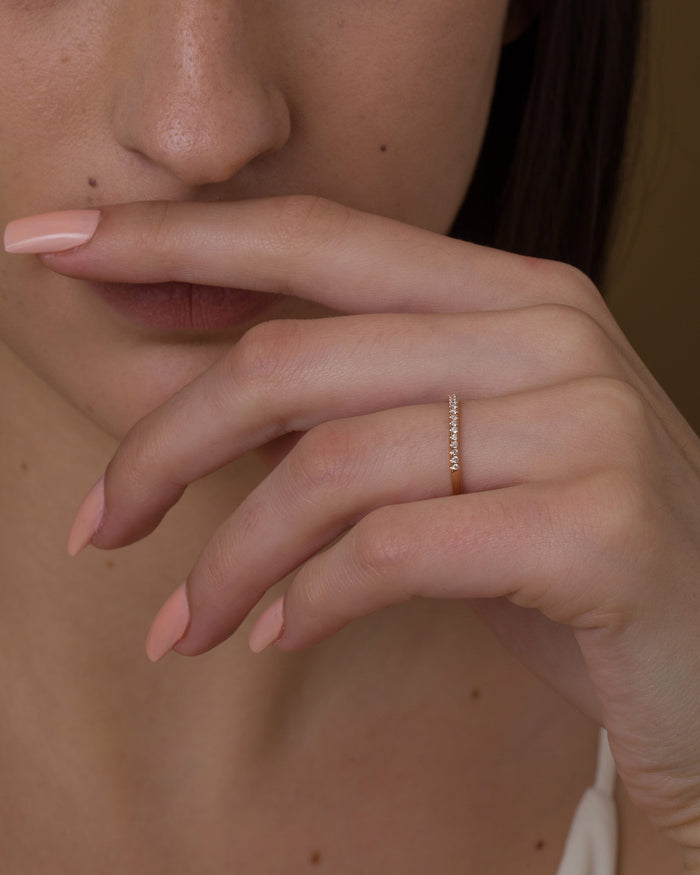 Dainty pave moissanite half eternity band in rose gold worn on a hand held near the face