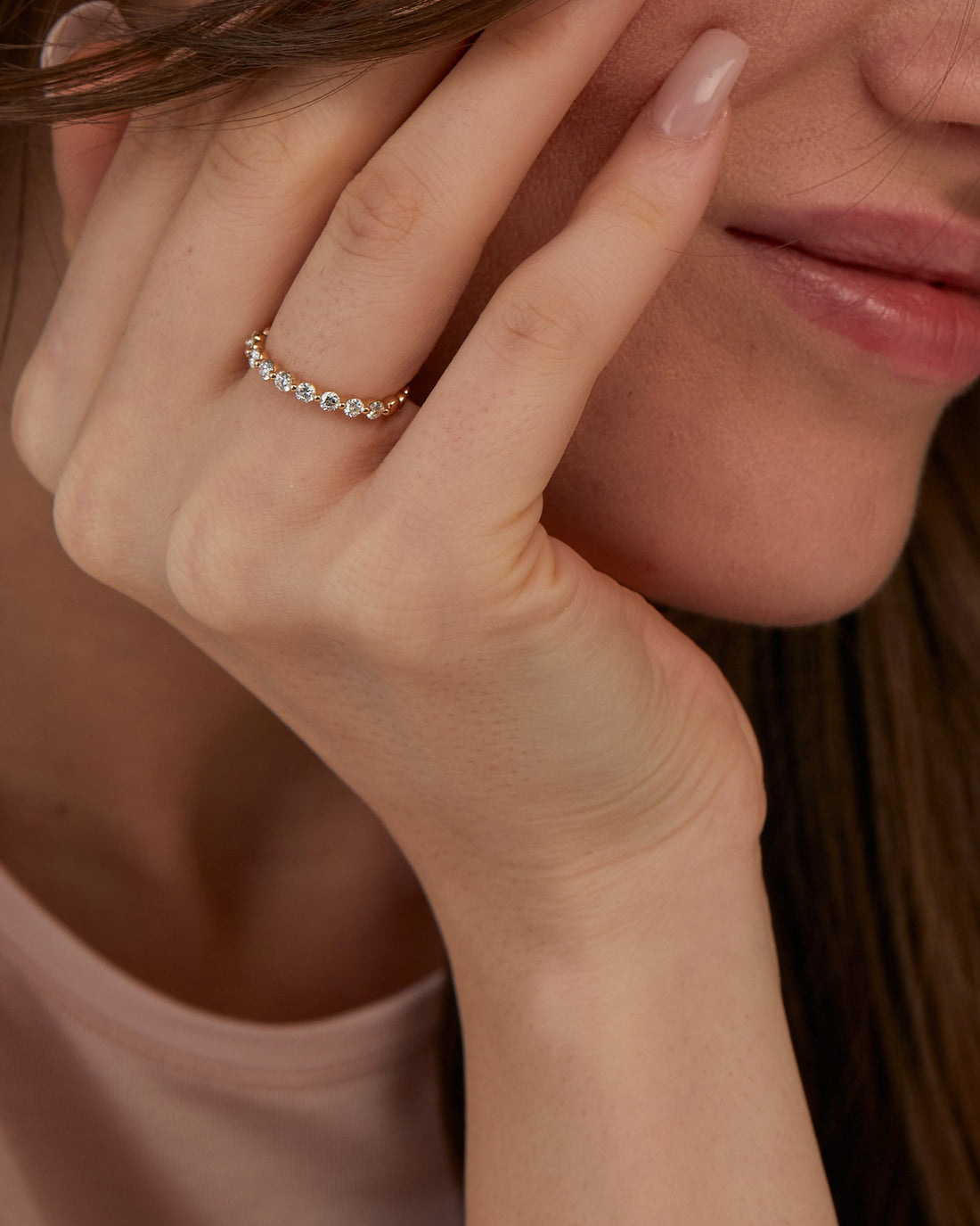 Round half eternity moissanite wedding band in rose gold worn on a hand held to the cheek