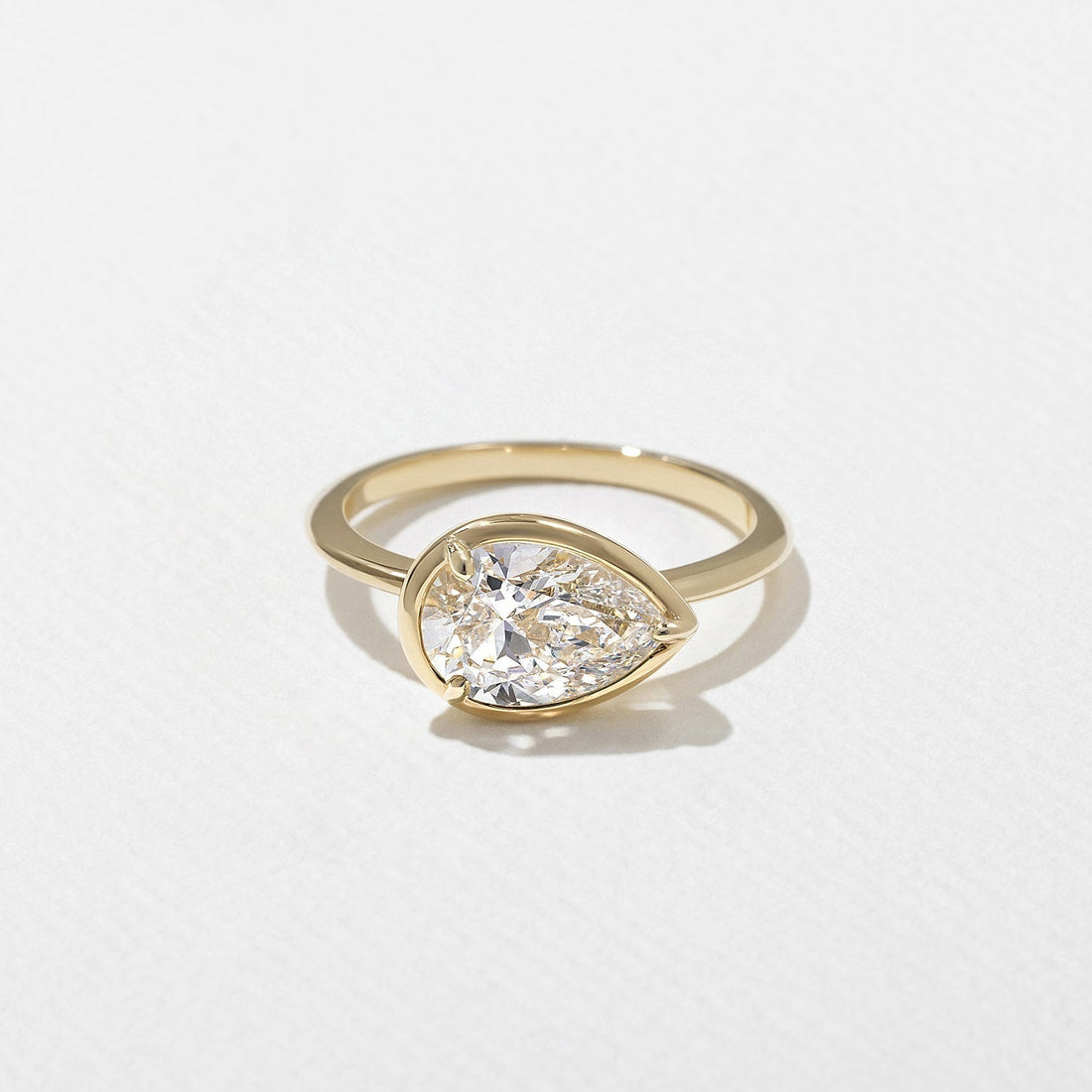 East west pear cut lab grown diamond bezel set engagement ring on a plain yellow gold band