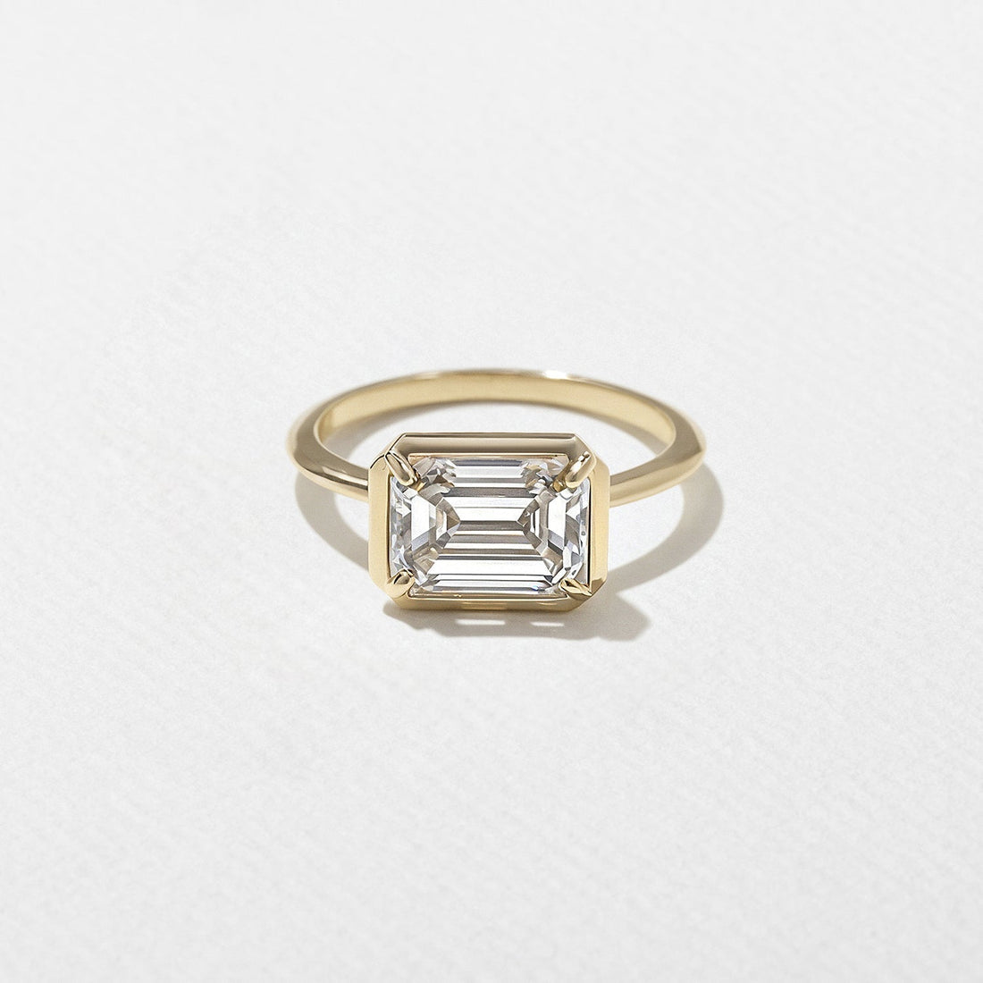 East west emerald cut lab grown diamond bezel set engagement ring on a plain yellow gold band