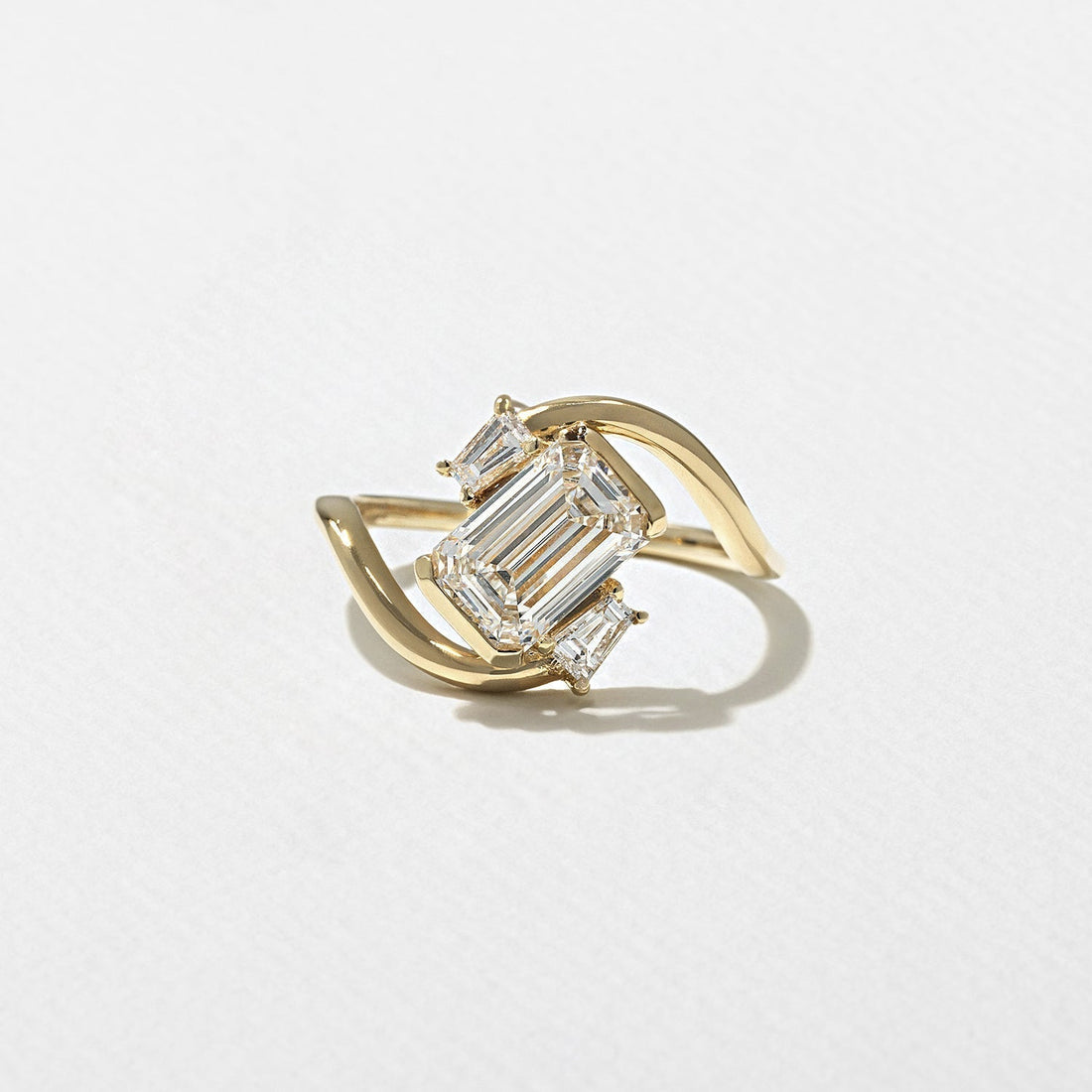 Emerald cut lab grown diamond sculptural swirl engagement ring with step cut accents in yellow gold
