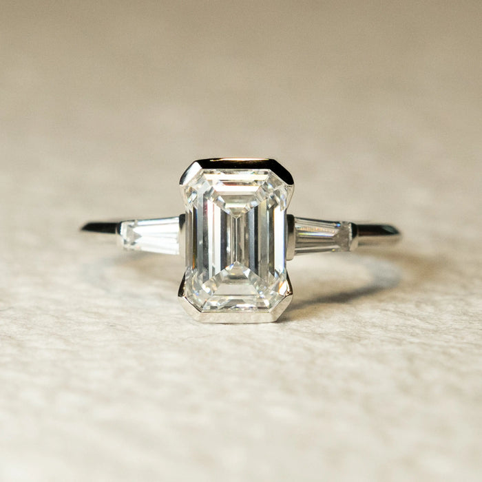 Emerald cut three stone moissanite engagement ring with half bezel in 14K gold