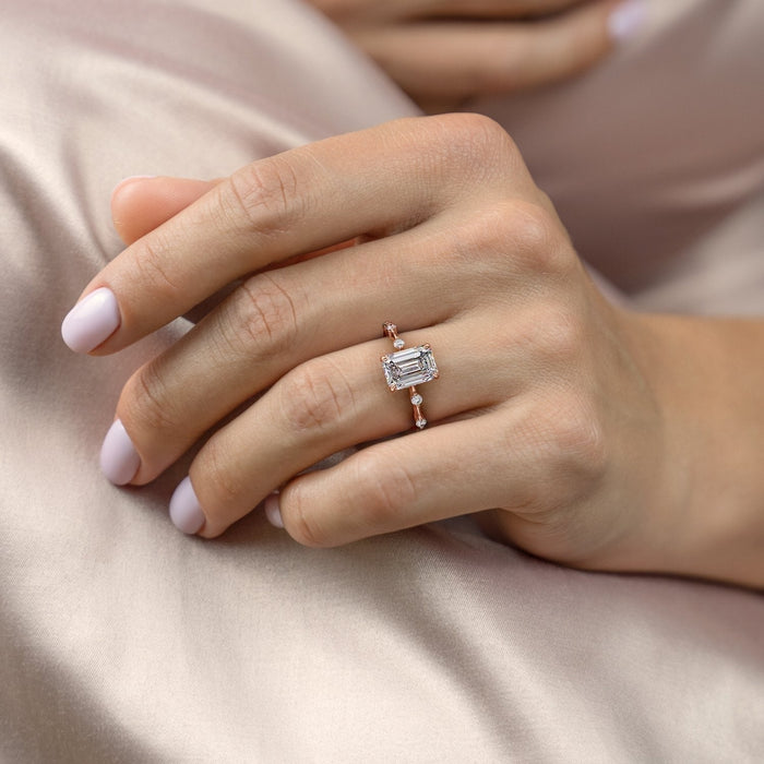 Emerald cut moissanite solitaire engagement ring with a hidden halo and a dainty band with spaced round stones